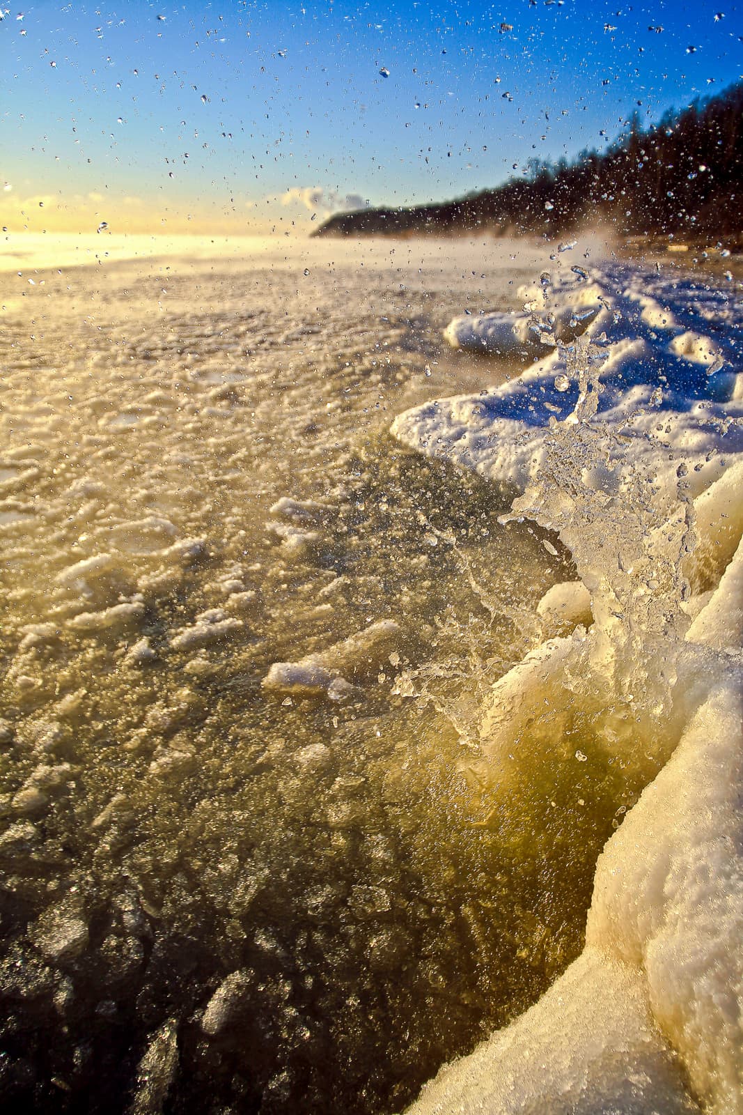 Water and ice shards spraying upward against a golden sunrise on a frozen Great Lakes shoreline