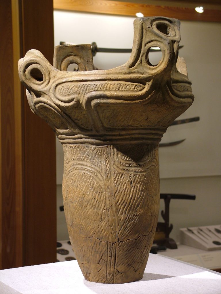 Photograph of a sculpture of a jar-like vase that is wider at the top where it opens up.