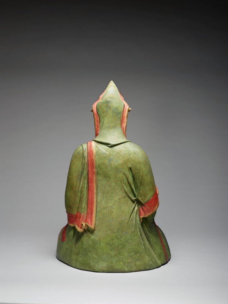 Photograph showing the back view of a sculpture of a person sitting; they are wearing a green and red robe.