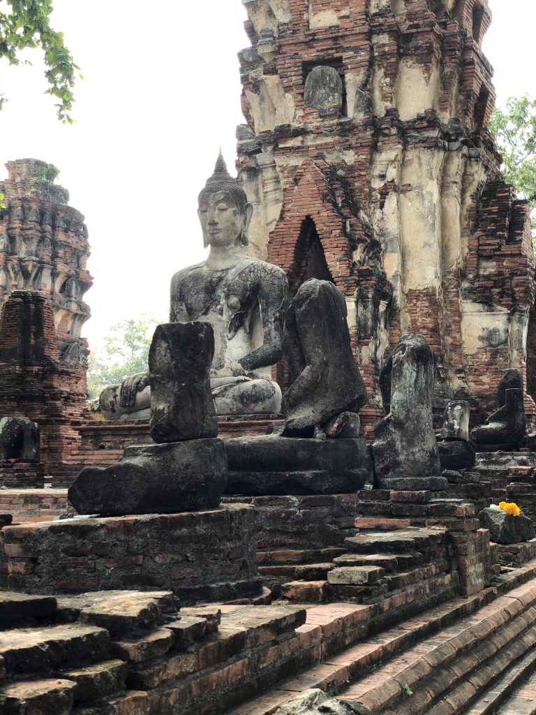 Photograph of the remains of a Buddhist temple. The temple is made of stone and has many large statues and structures but is worn and has damage to the stone.