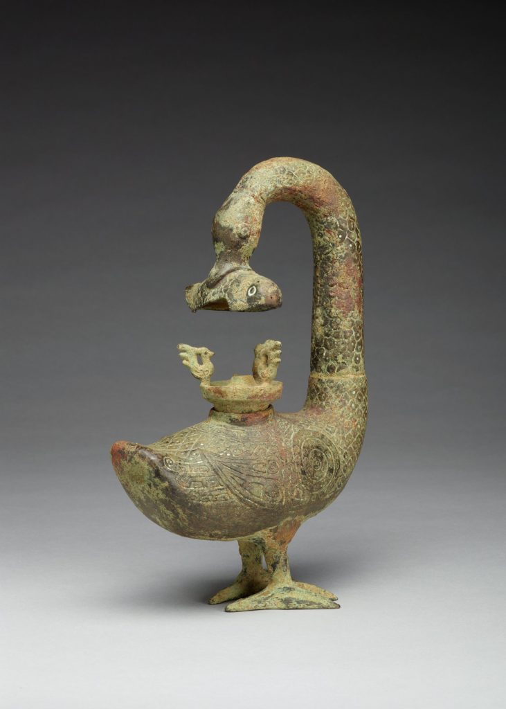 Photograph of a sculpture depicting a goose with its neck bent all of the way around to its back, it is holding something in its mouth.