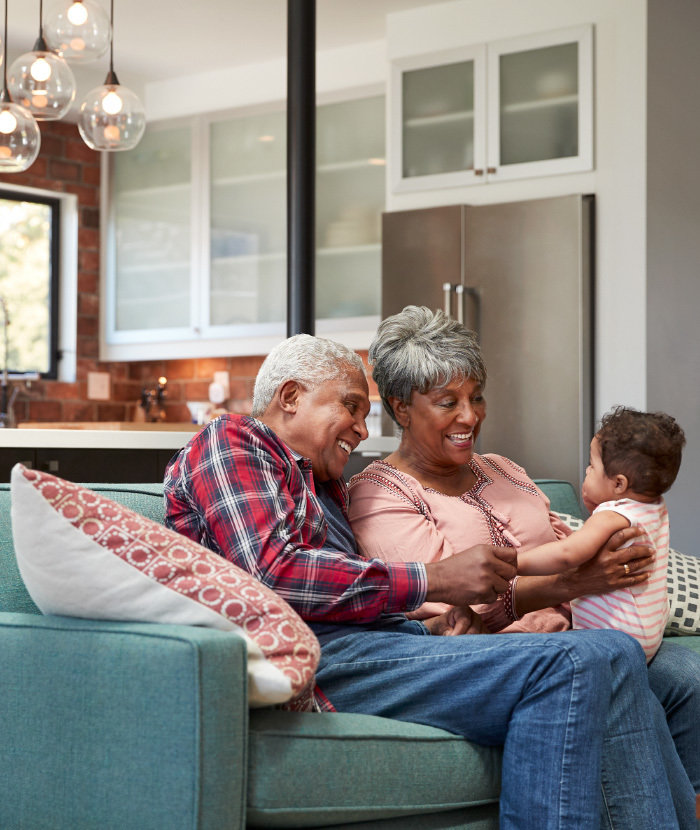 Older couple play with a young grandchild on a couch