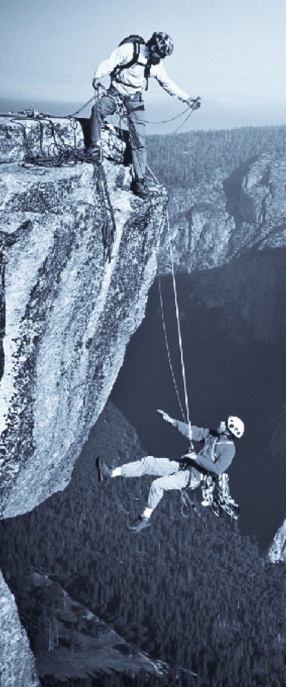 Two climbers: one secures the other who is hanging over the abyss with a rope