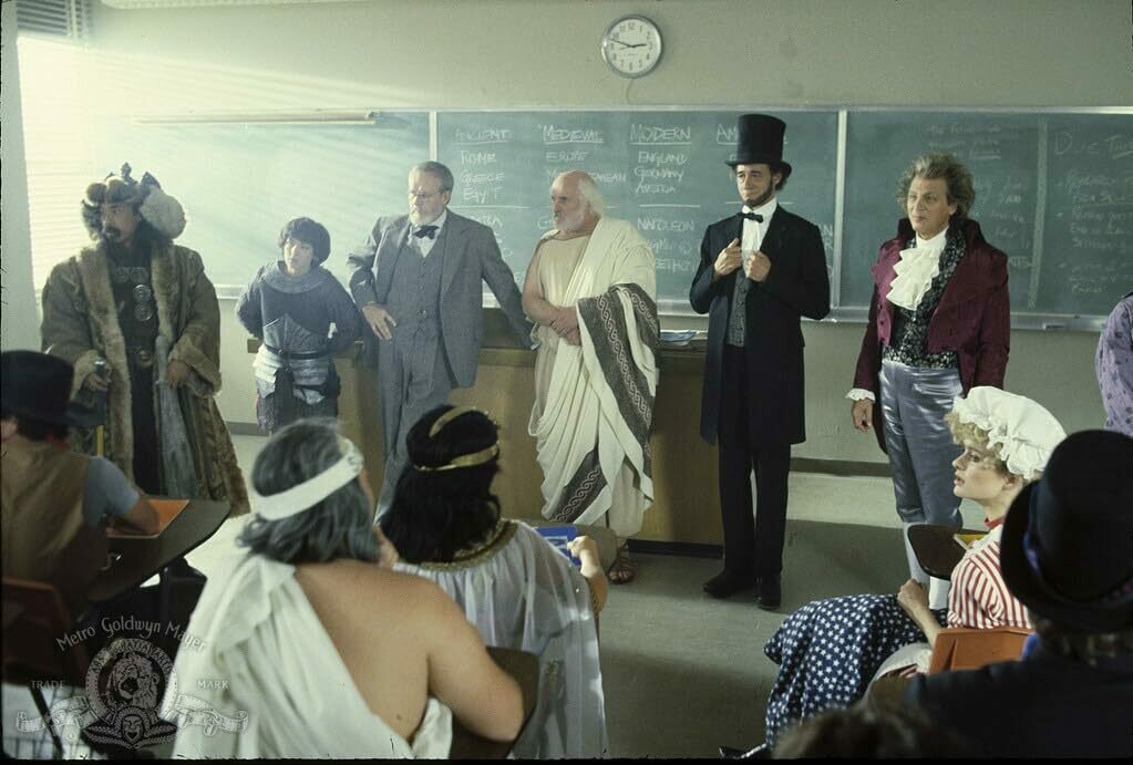 Historical figures standing at the front of a classroom looking at the class. Includes Beethoven, Abraham Lincoln, Socrates, Sigmund Freud, Joan of Arc and Genghis Khan