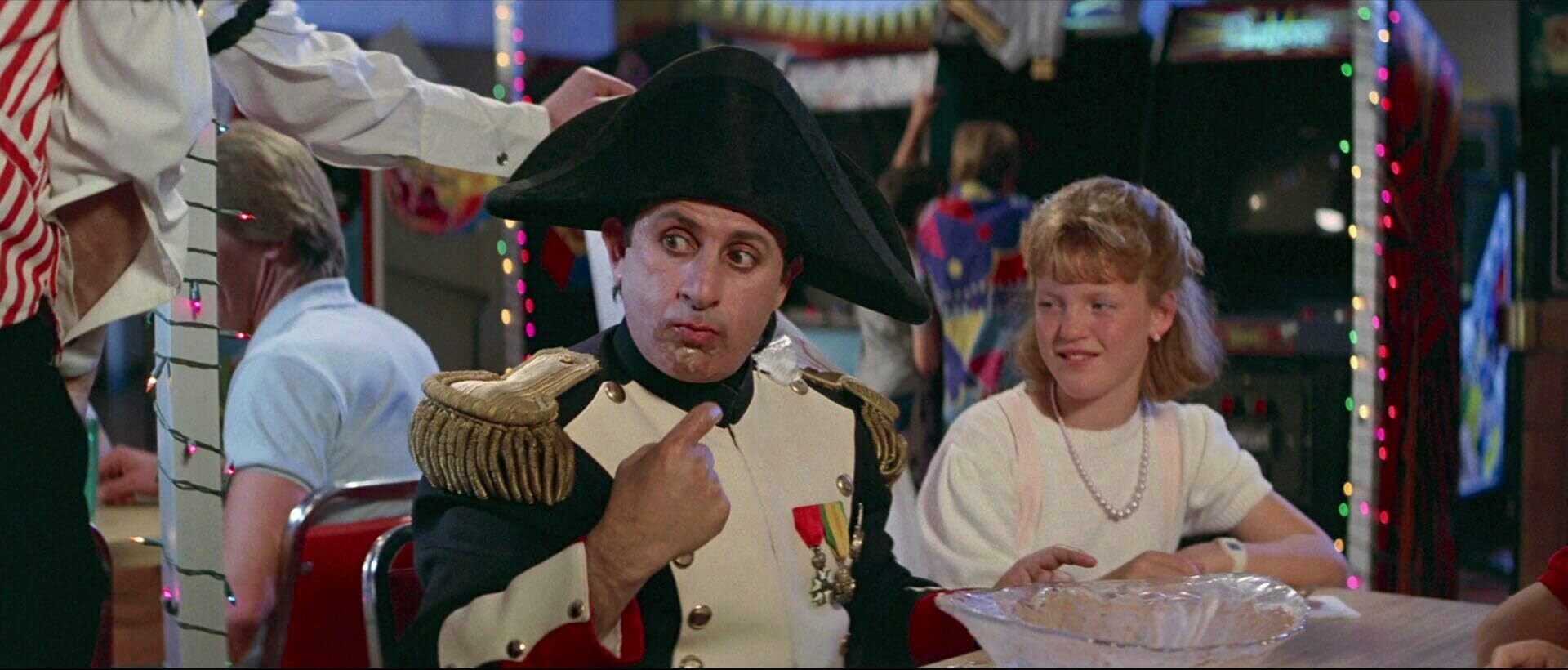 Napoleon at a buffet having just eaten a big bowl of ice cream. He's still got ice cream on his chin and has eyes wide in a weird expression. He's wearing typical Napoleon fare
