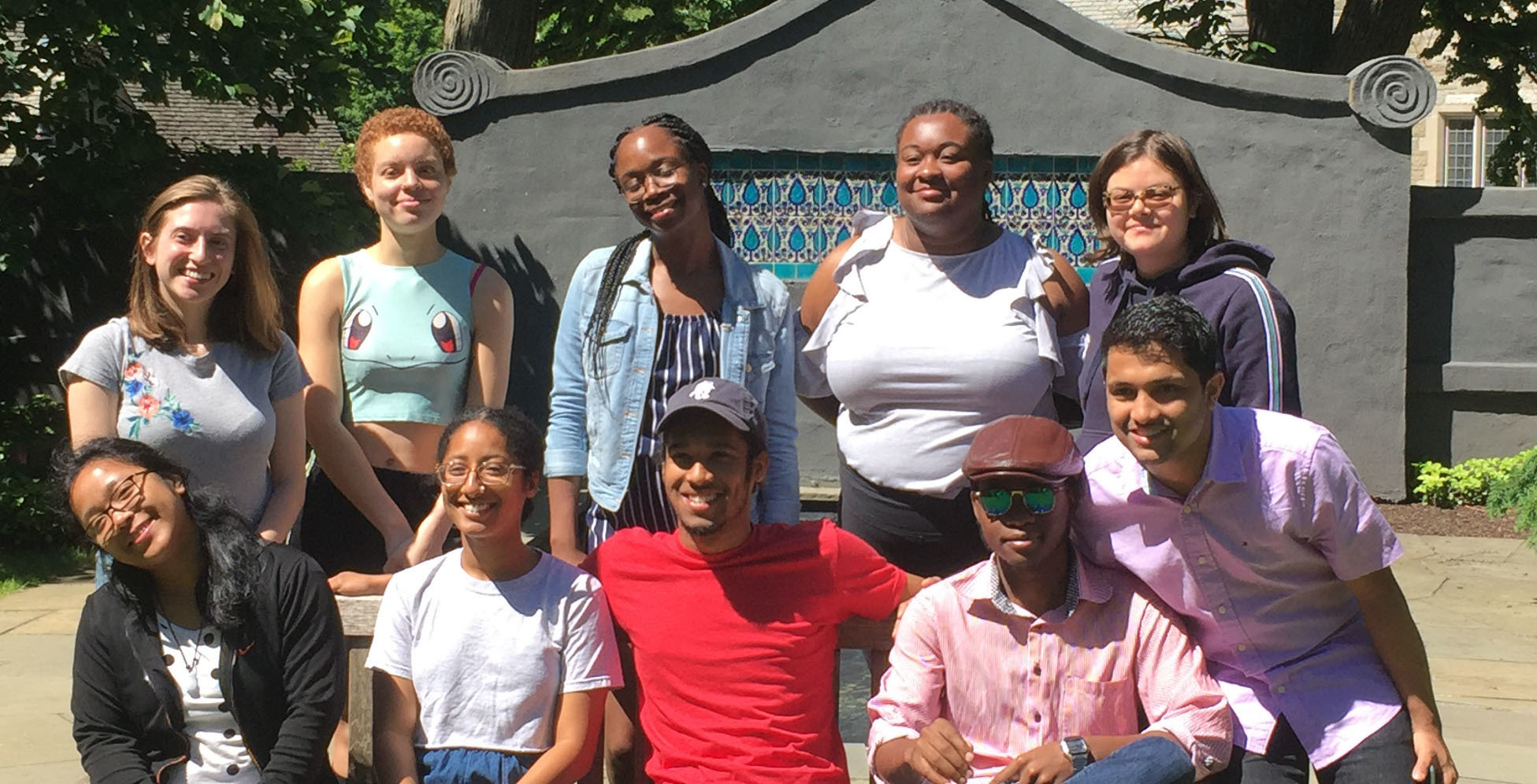 ten students pose in front of a stone wall with tile inlay