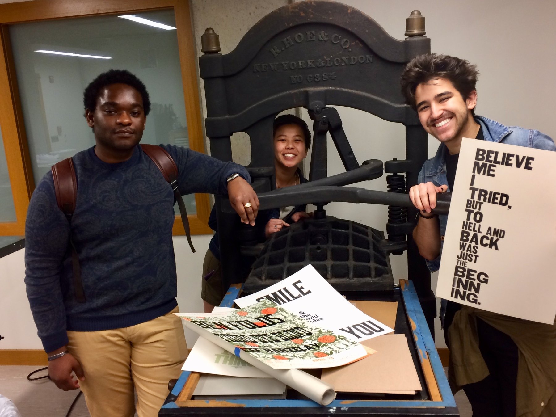 three students pose with a letterpress and prints