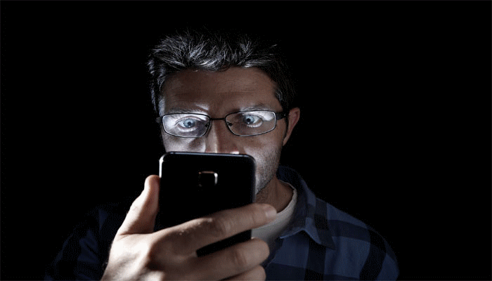Sleep Hygiene - a smartphone screen glowing brightly in a pitch-black room, reflecting in a person’s eyes.