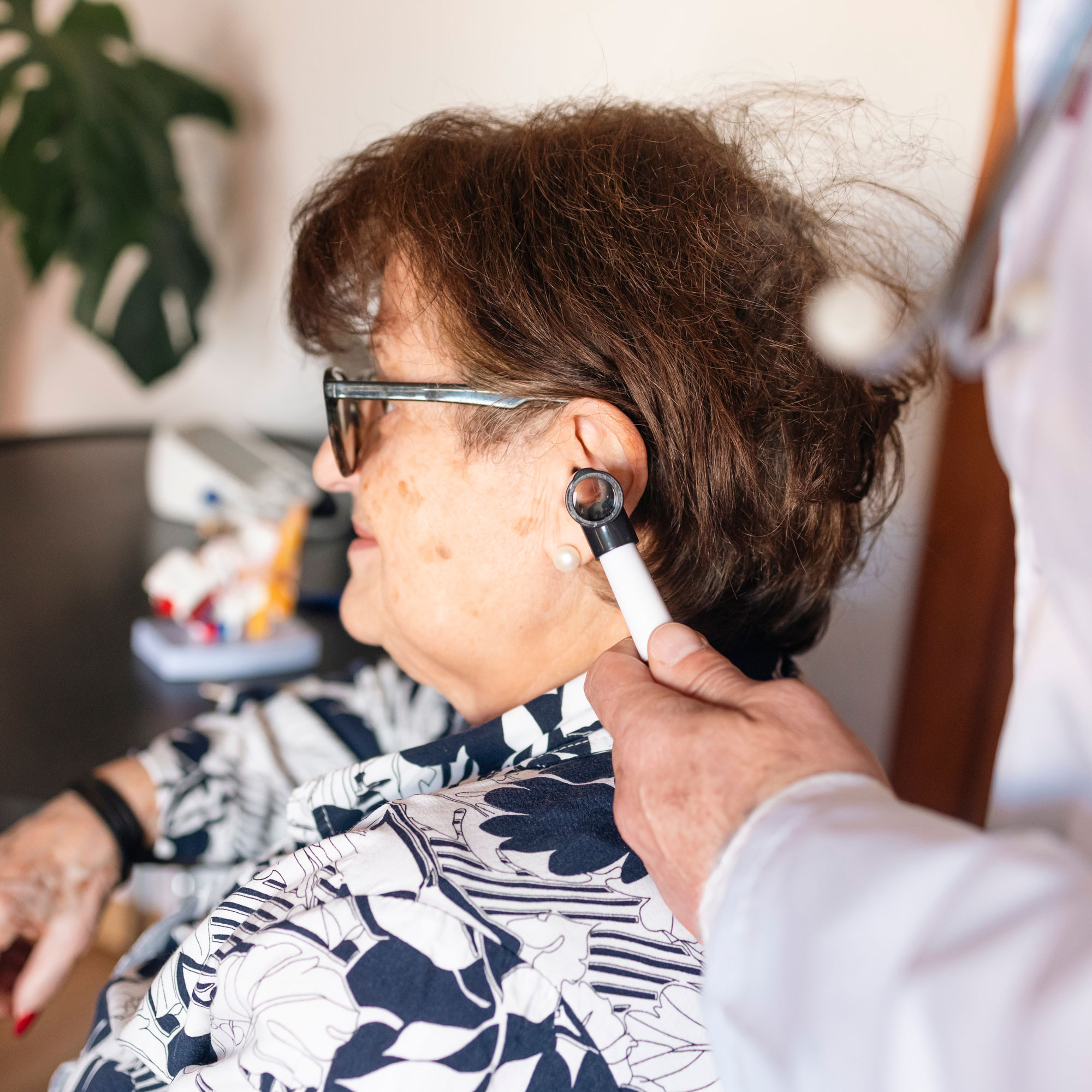Doctor using otoscope examining ear of senior woman patient during medical consultation in home