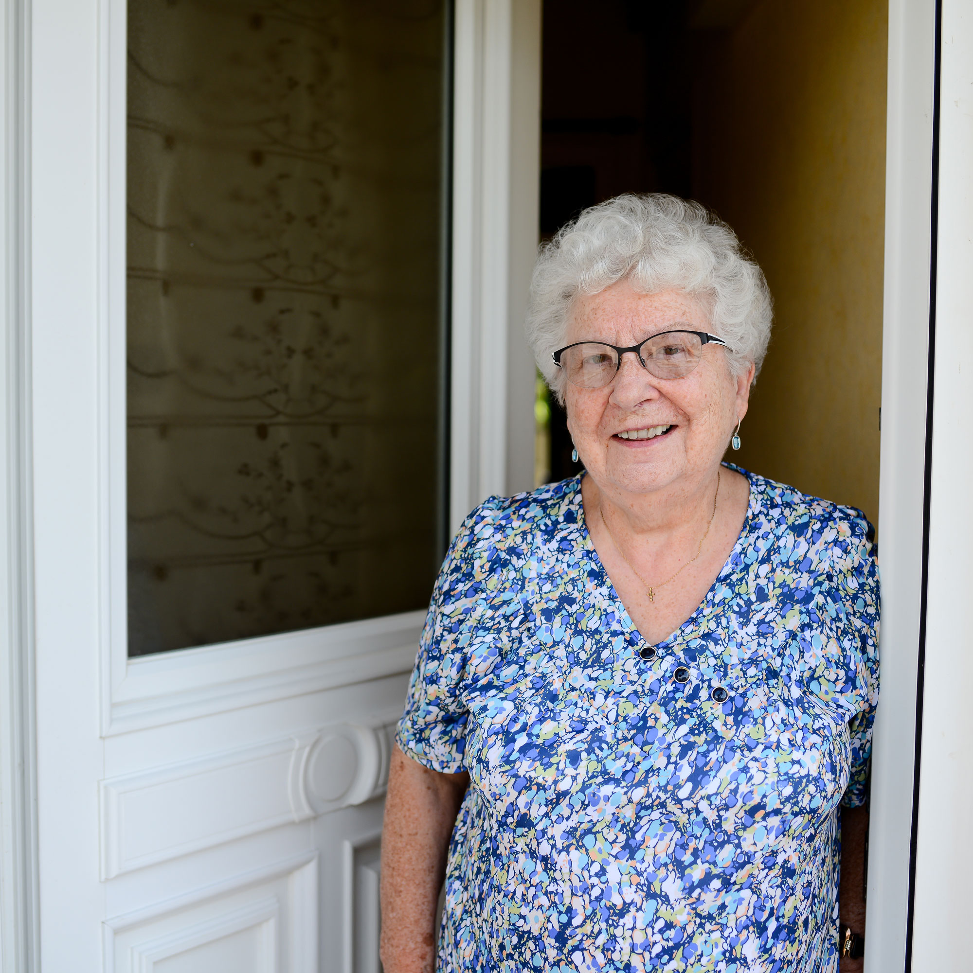 elderly senior woman opening front door of house and welcoming people at home