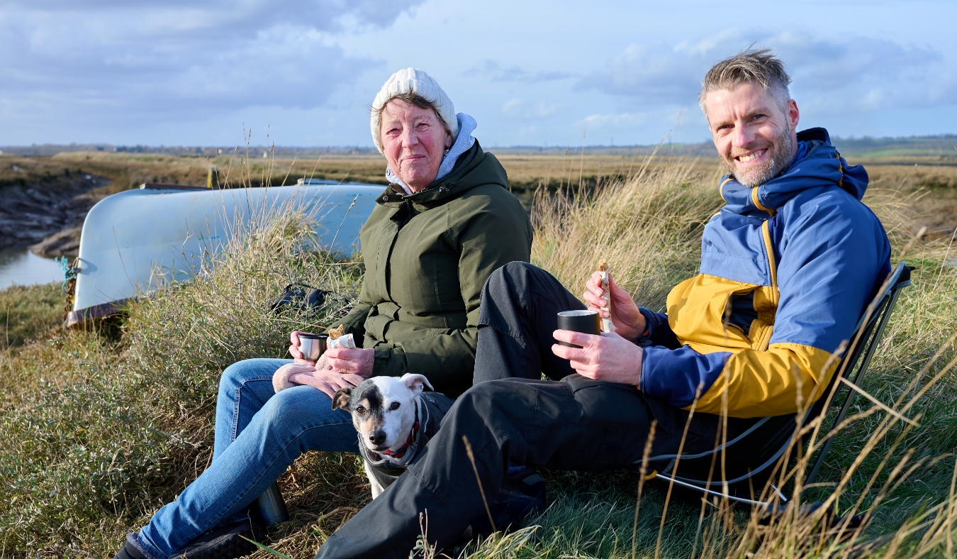 elderly mother and adult son enjoying a warm meal by the water