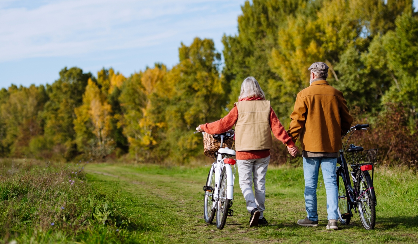 elderly couple on a walk in the forest pushing their bikes side by side