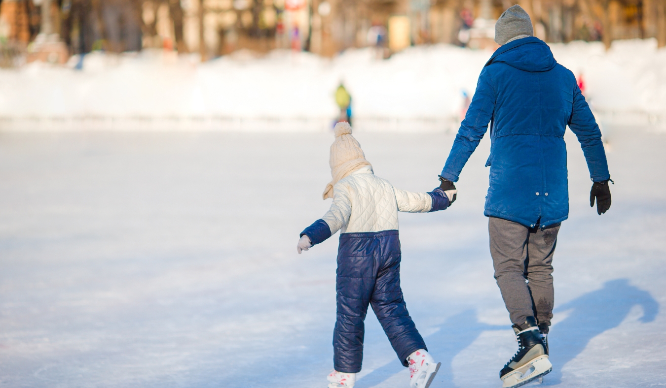 girl with father learning to skate on ice rink