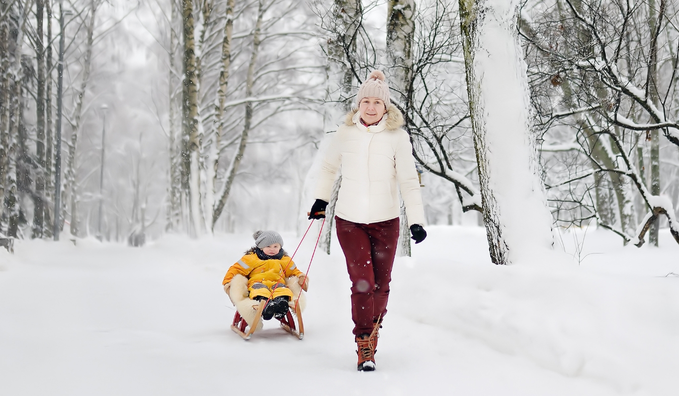 grandmother pulling grandchild on sled in snow