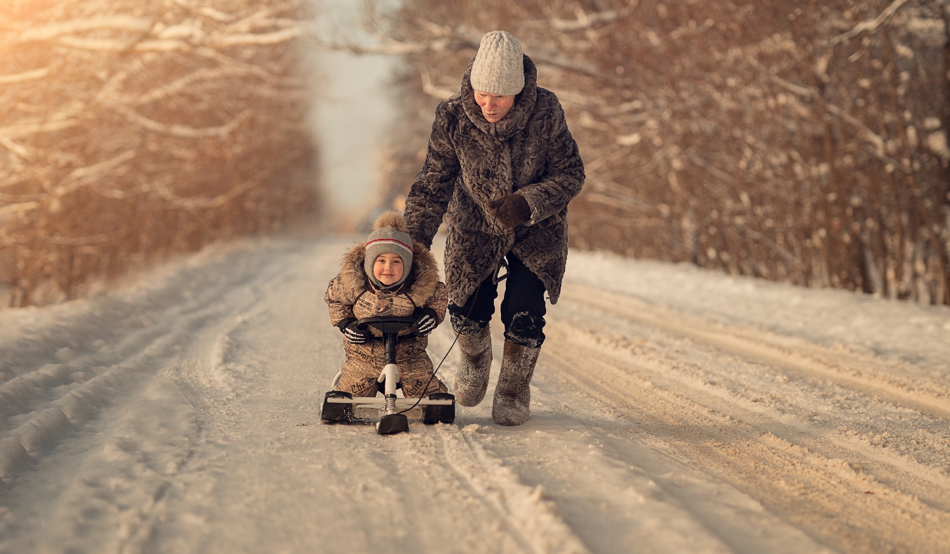 grandmother pushing grandchild on snow sled