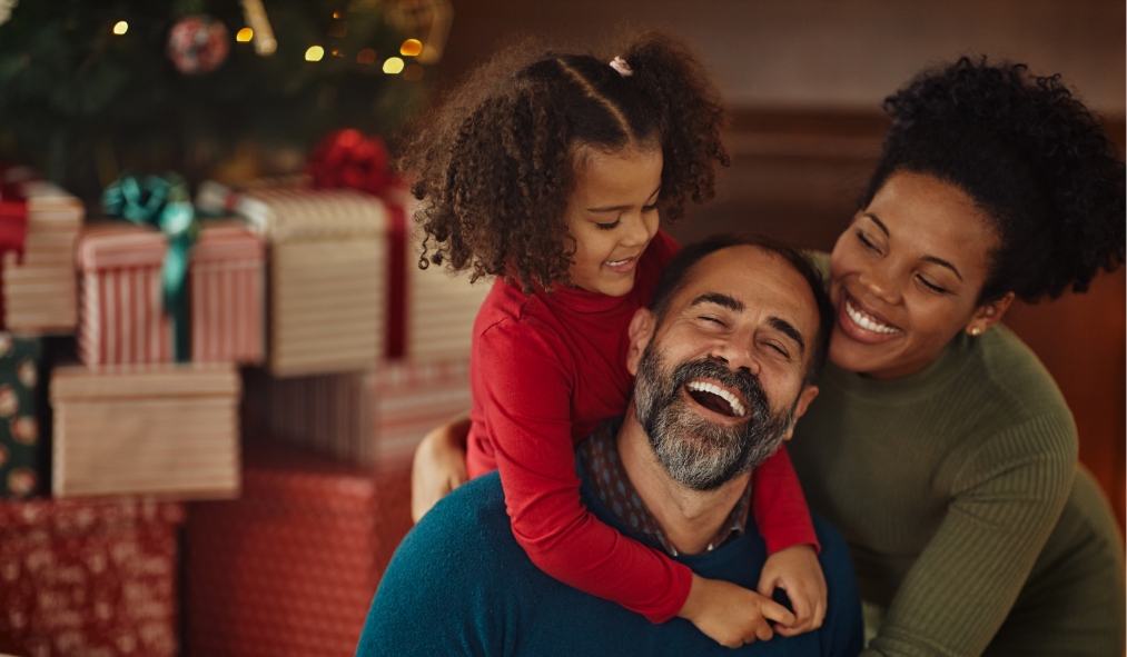 events christmas black family hugging by christmas tree with gifts