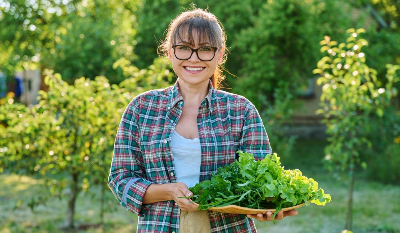 woman holding basket of harvested lettuce greens from garden