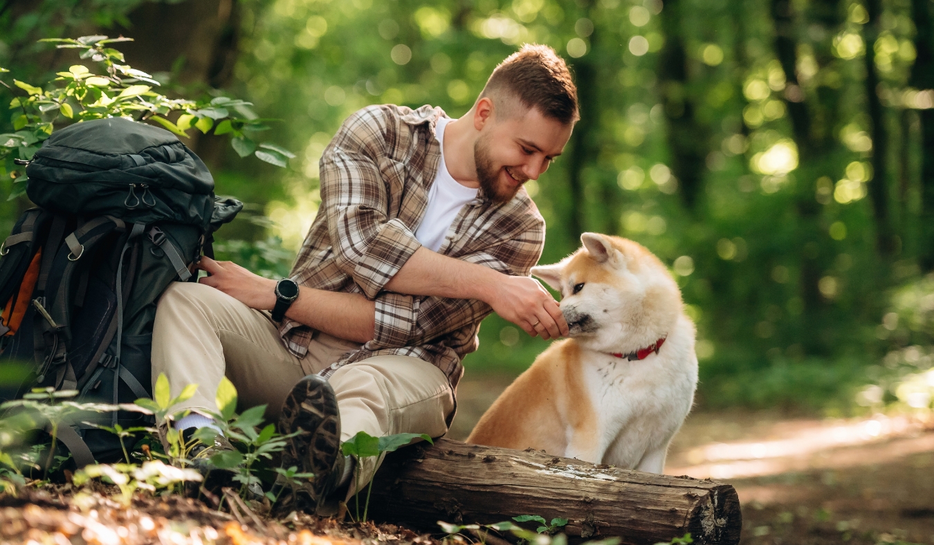 man feeding pet dog treat during hike