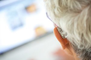 white haired man head with hearing aid in ear