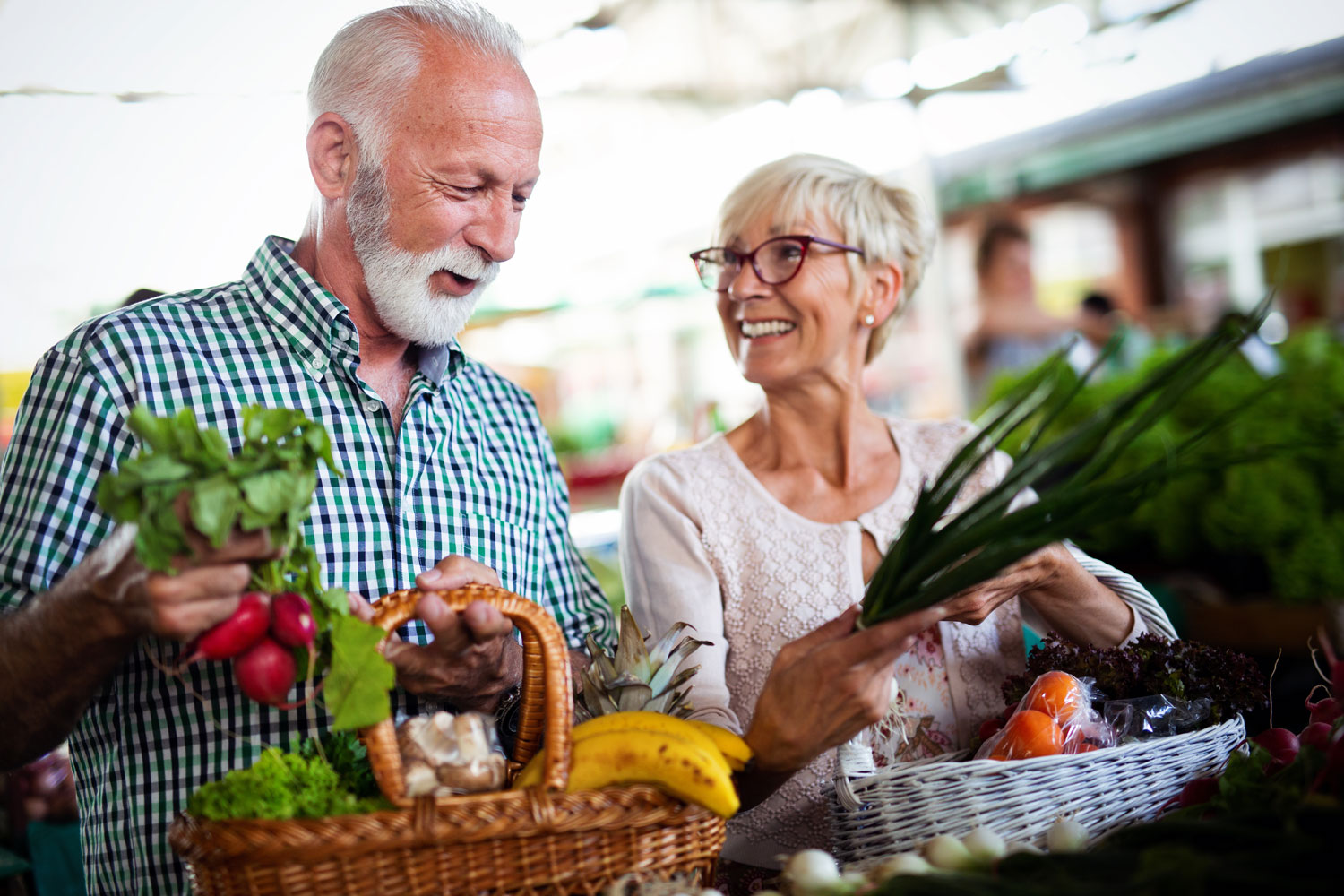 smiling senior couple holding basket with vegetables at the market