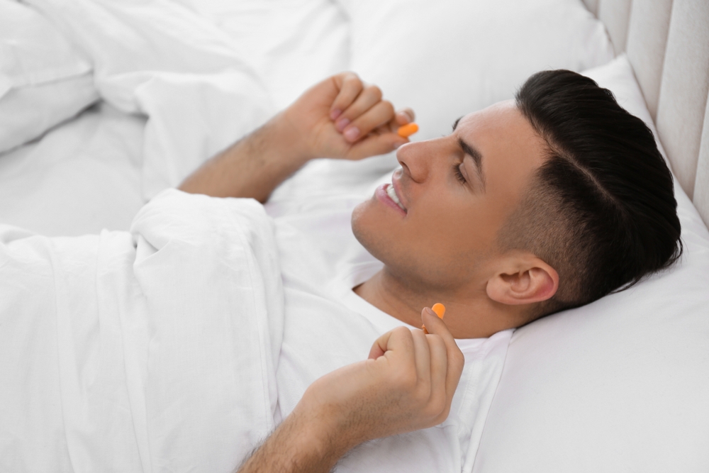Man,Inserting,Foam,Ear,Plugs,In,Bed