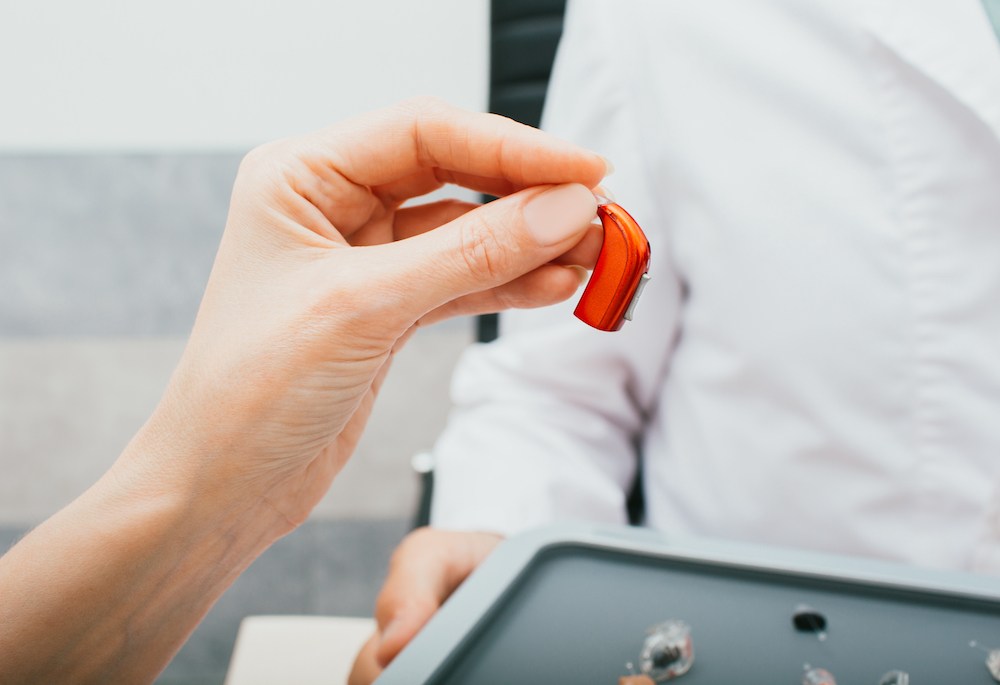 hand holding a red bte hearing aid device