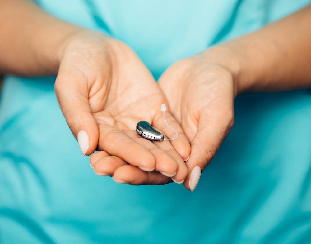 hand holding a single silver bte hearing aid
