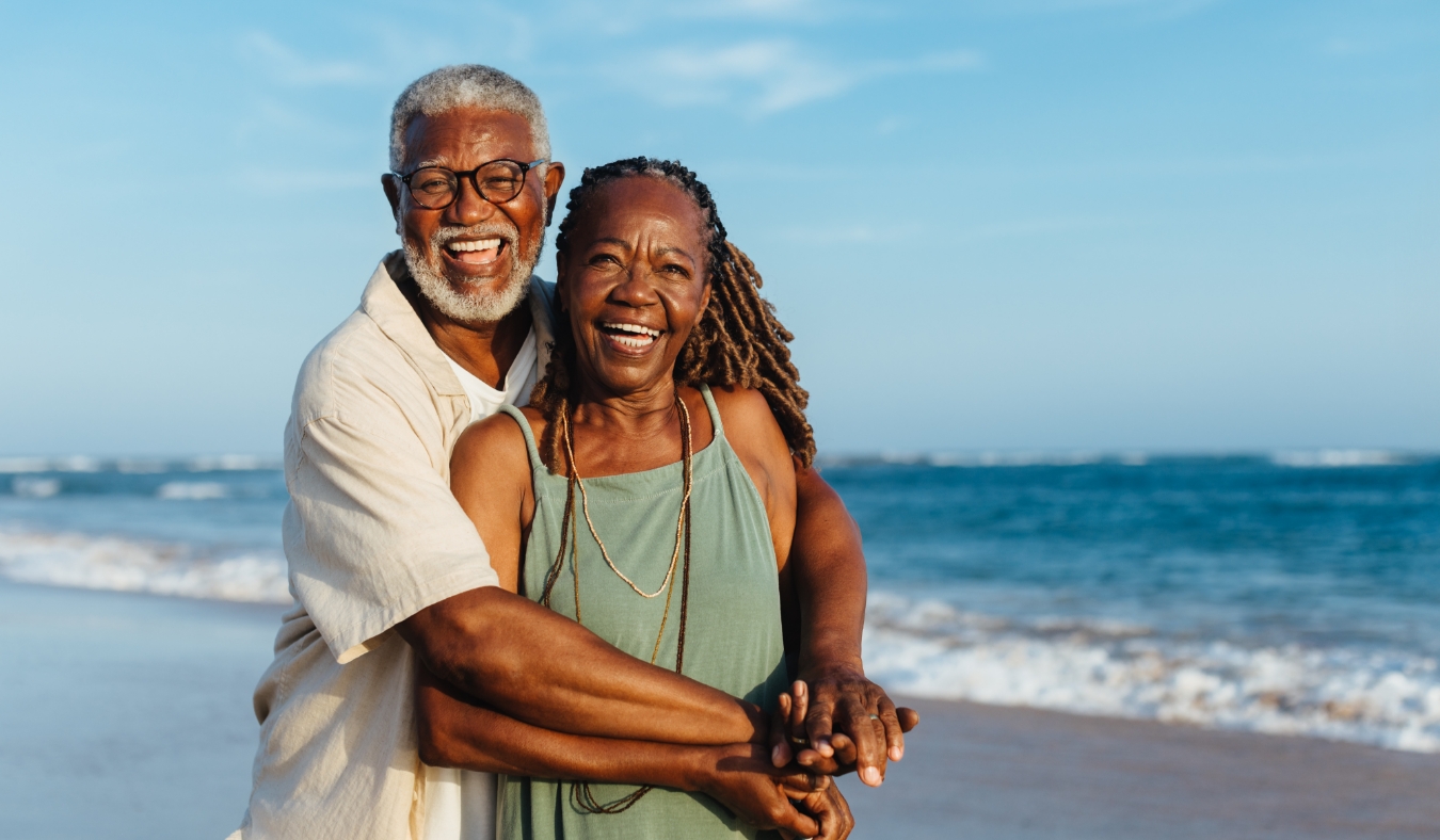 An older African American couple embrace warmly during a joyful walk along a sandy beach