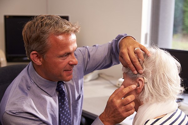 a hearing specialist performing a hearing aid fitting for his elderly patient