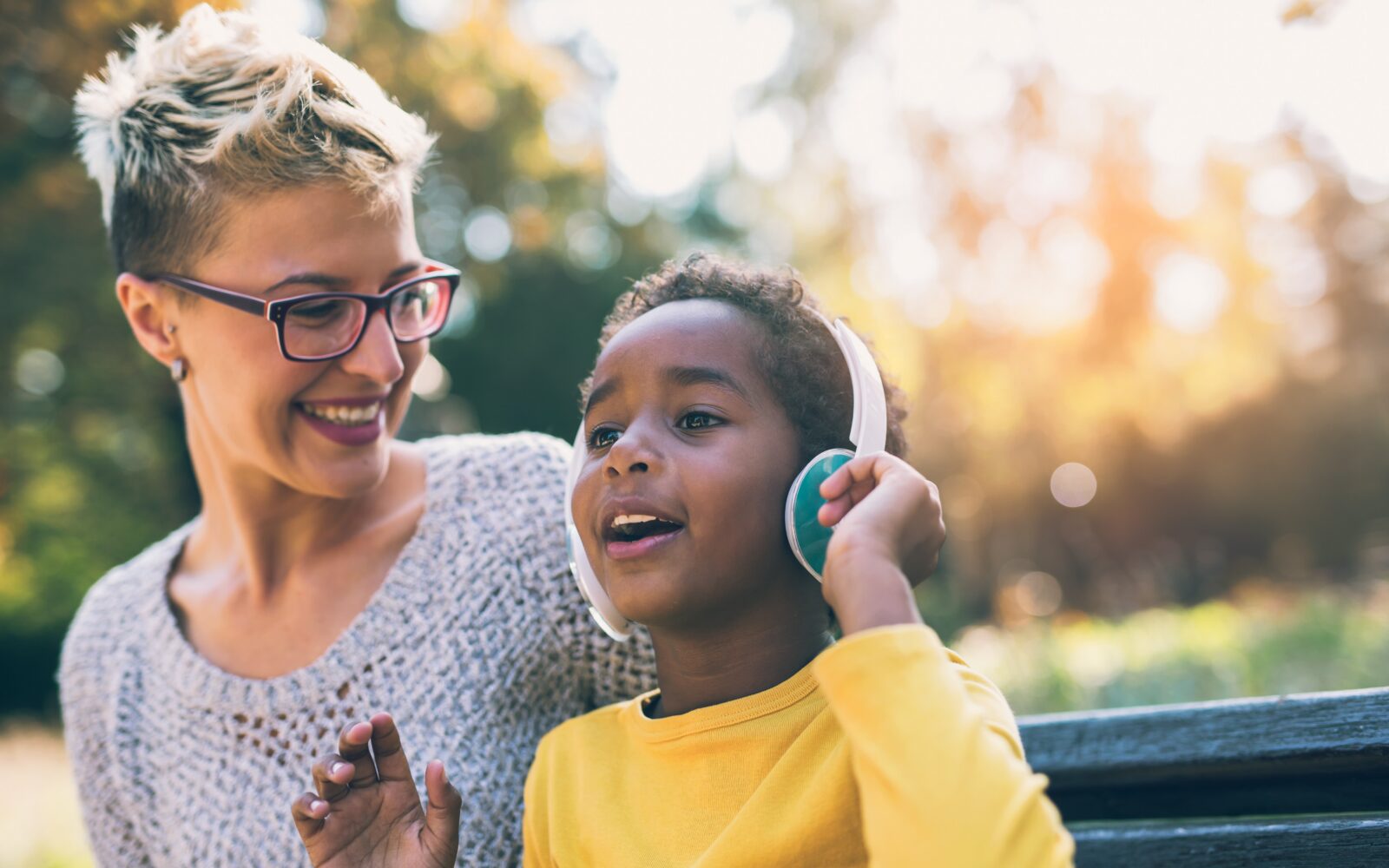 Smiling mother and little daughter having fun, listening to music on headphones Mixed race family
