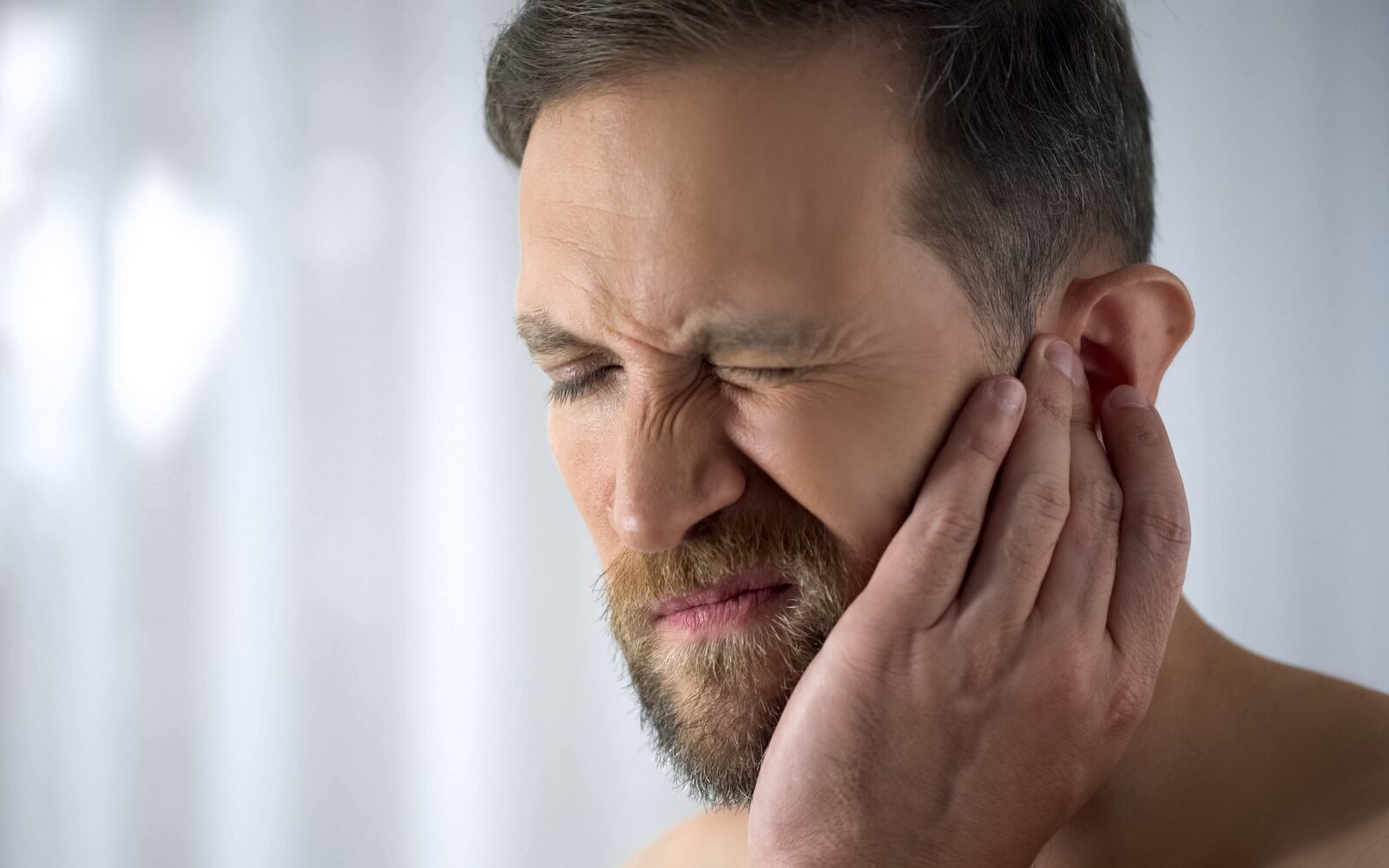 Man holding his aching ear, suffering from otitis, sudden hearing loss, close up