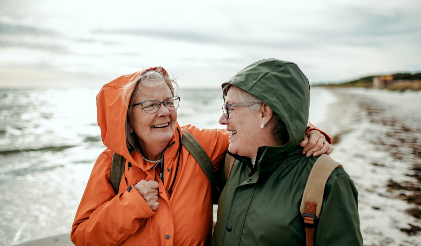 two senior friends walking on a chilly beach