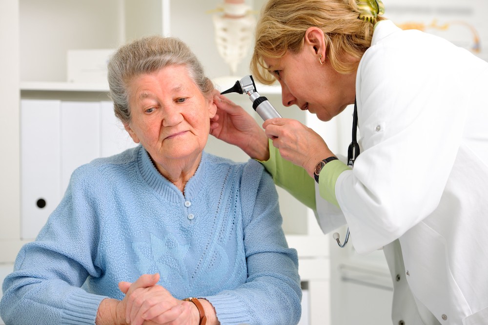 audiologist using hearing instrument to examine inner ear canal of her patient