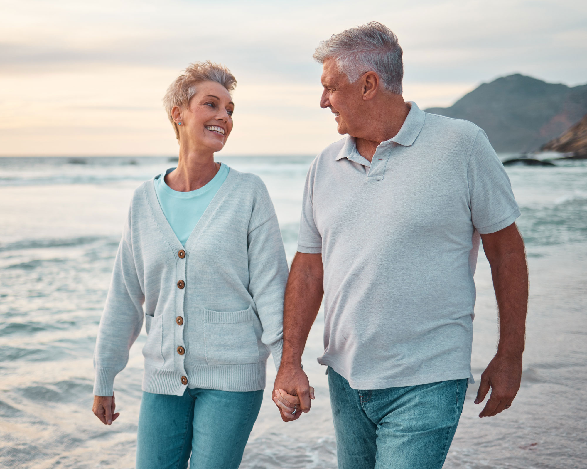 senior couple holding hands walking along beach