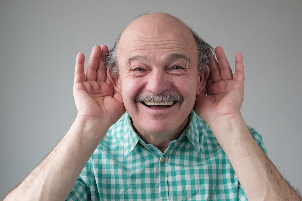 goofy looking man holding both hands to his ears