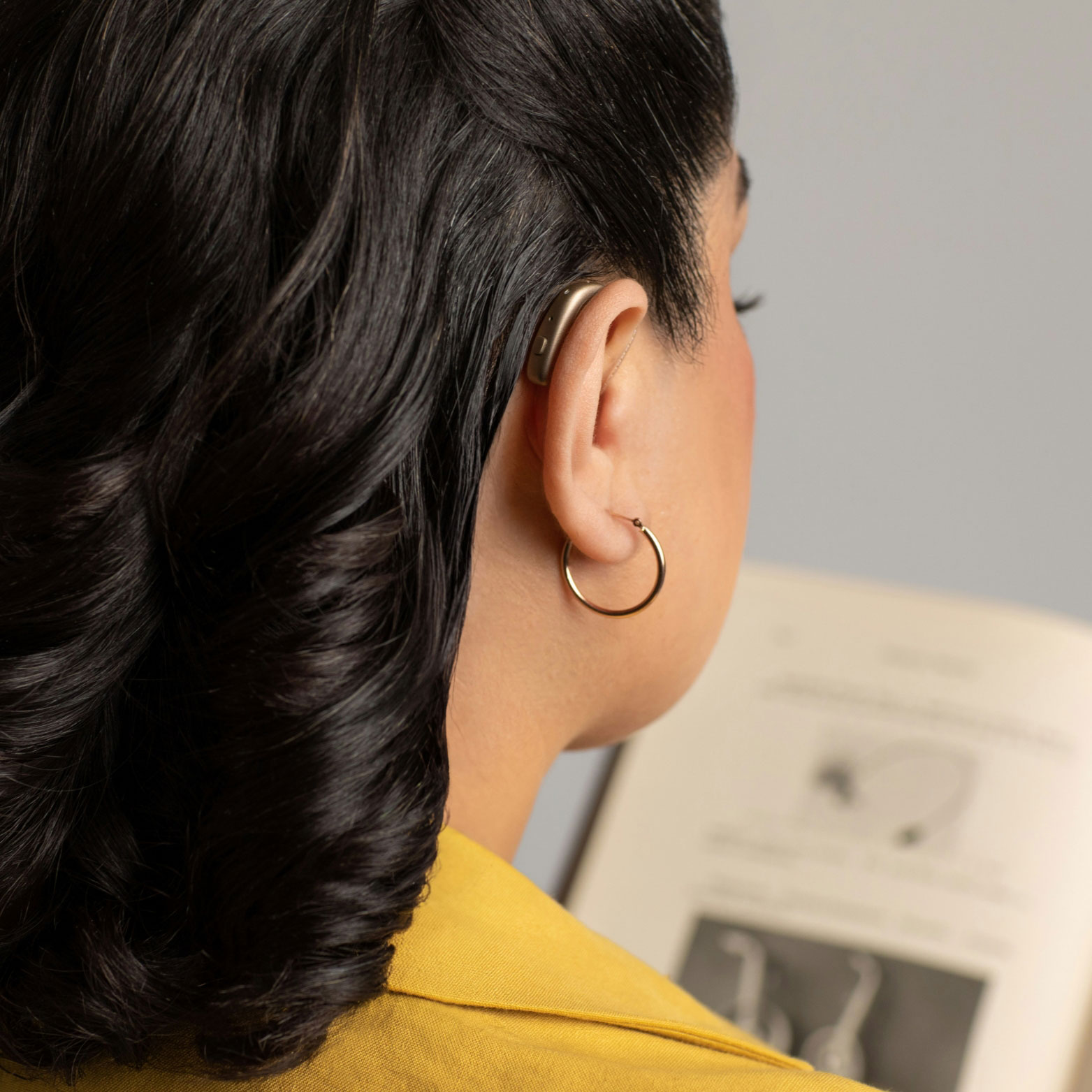 gn woman wearing hearing aid while reading sq