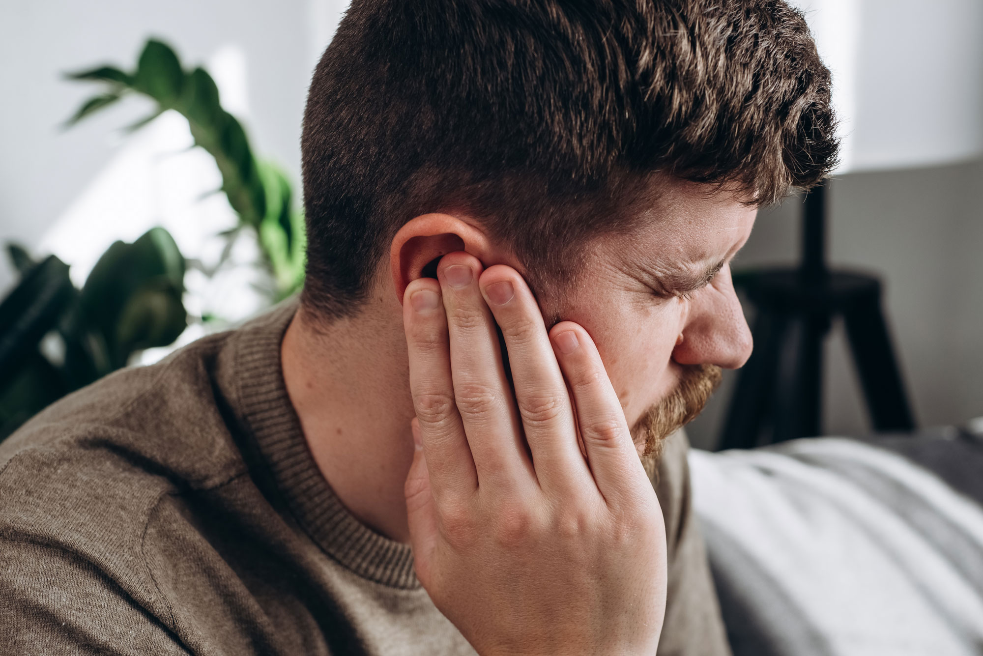 man holding hand to ear due to tinnitus ringing