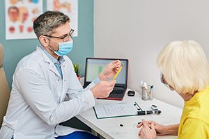 audiologist in mask discussing treatment services with his patient in office