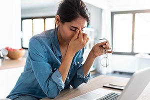 image of a woman sitting at a laptop pinching the bridge of her nose