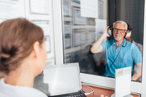 patient in blue polo shirt smiling while having hearing tested by professional