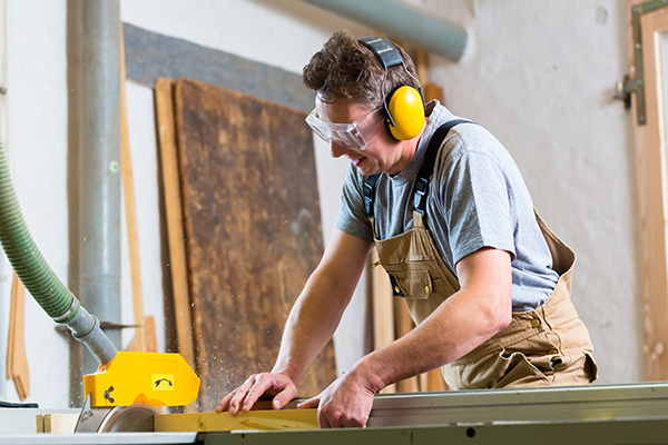 middle aged man cutting wood while wearing yellow over-the-head hearing protection