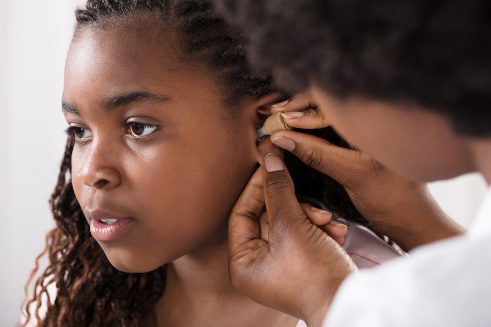 young woman looking forward as her hearing specialist fits a hearing aid device