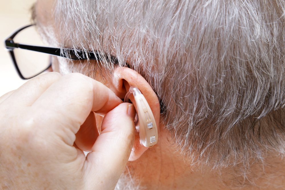 man inserting a tan colored hearing aid to his left ear