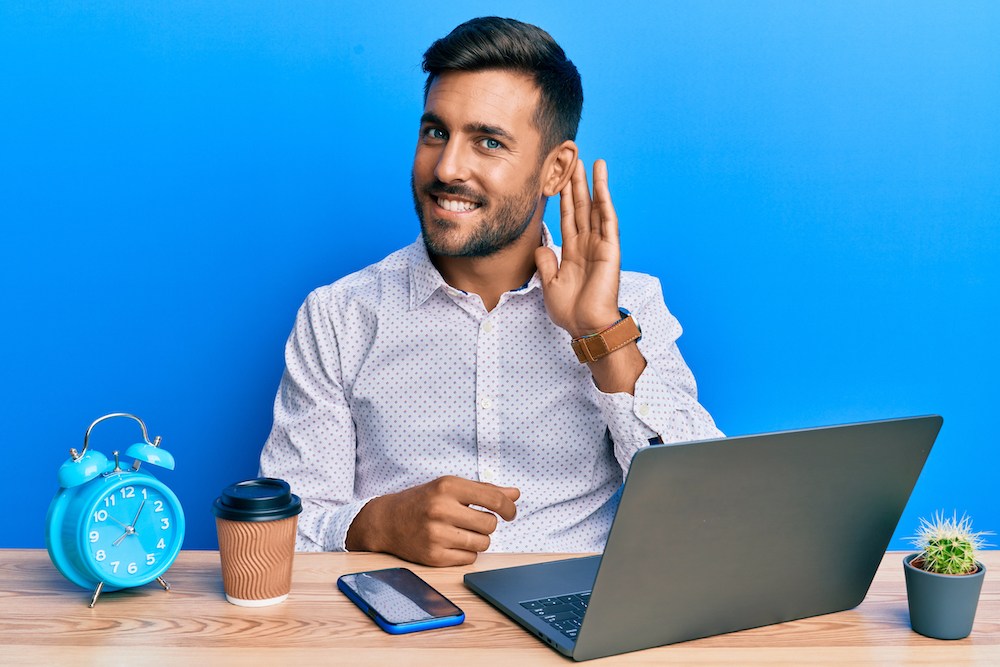 man expressively gesturing towards his ear while working from home