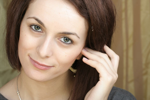 a smirking woman holding a hand to her ear