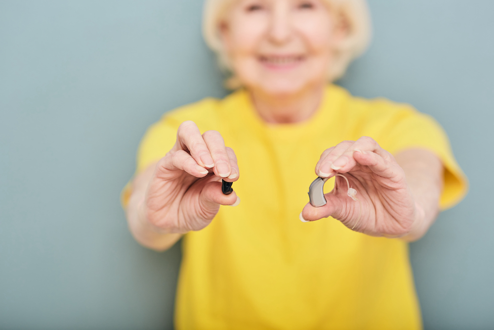 woman in yellow shirt holding two hearing aids