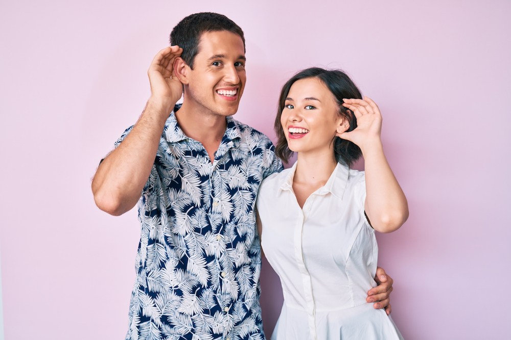 smiling couple gesturing towards their ears
