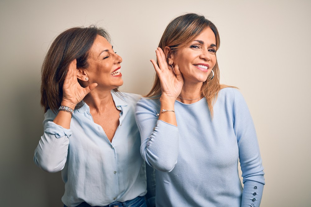 two professionally dressed women holding hands to ears