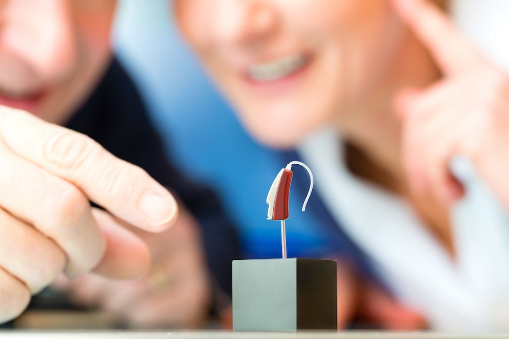 two patients looking at a premium hearing aid device on a display stand