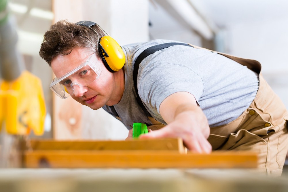 man in his garage cutting wood while wearing yellow over the ears protectors